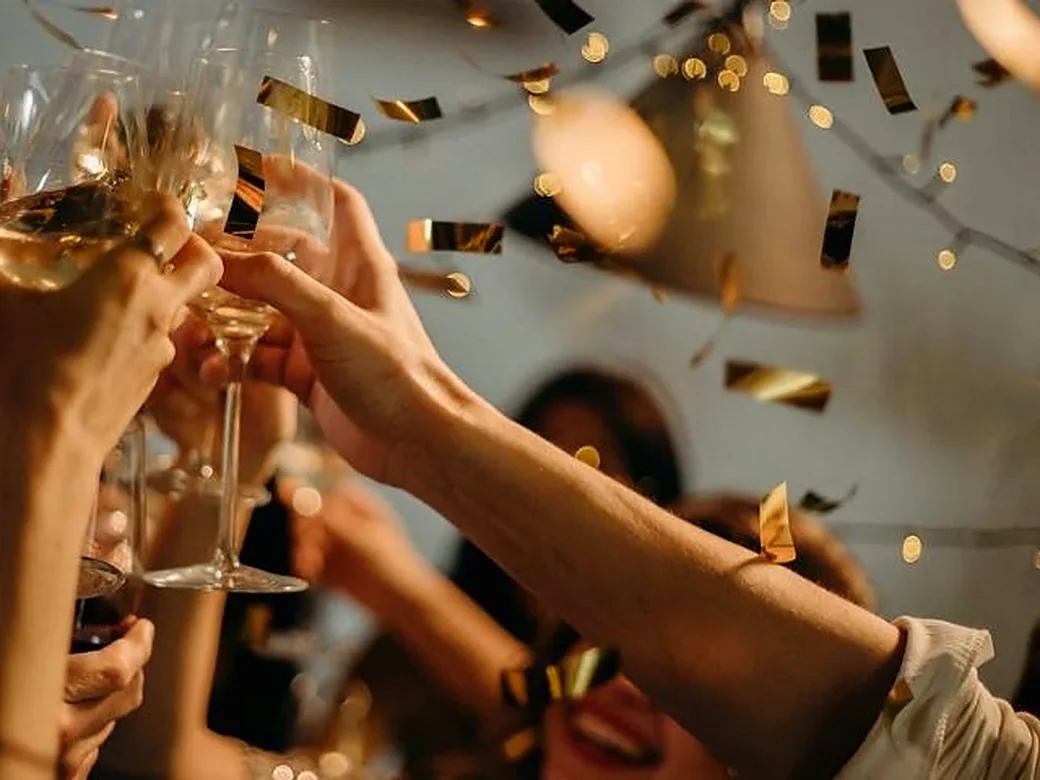 Brinde de taças erguidas sob luzes e confete dourado