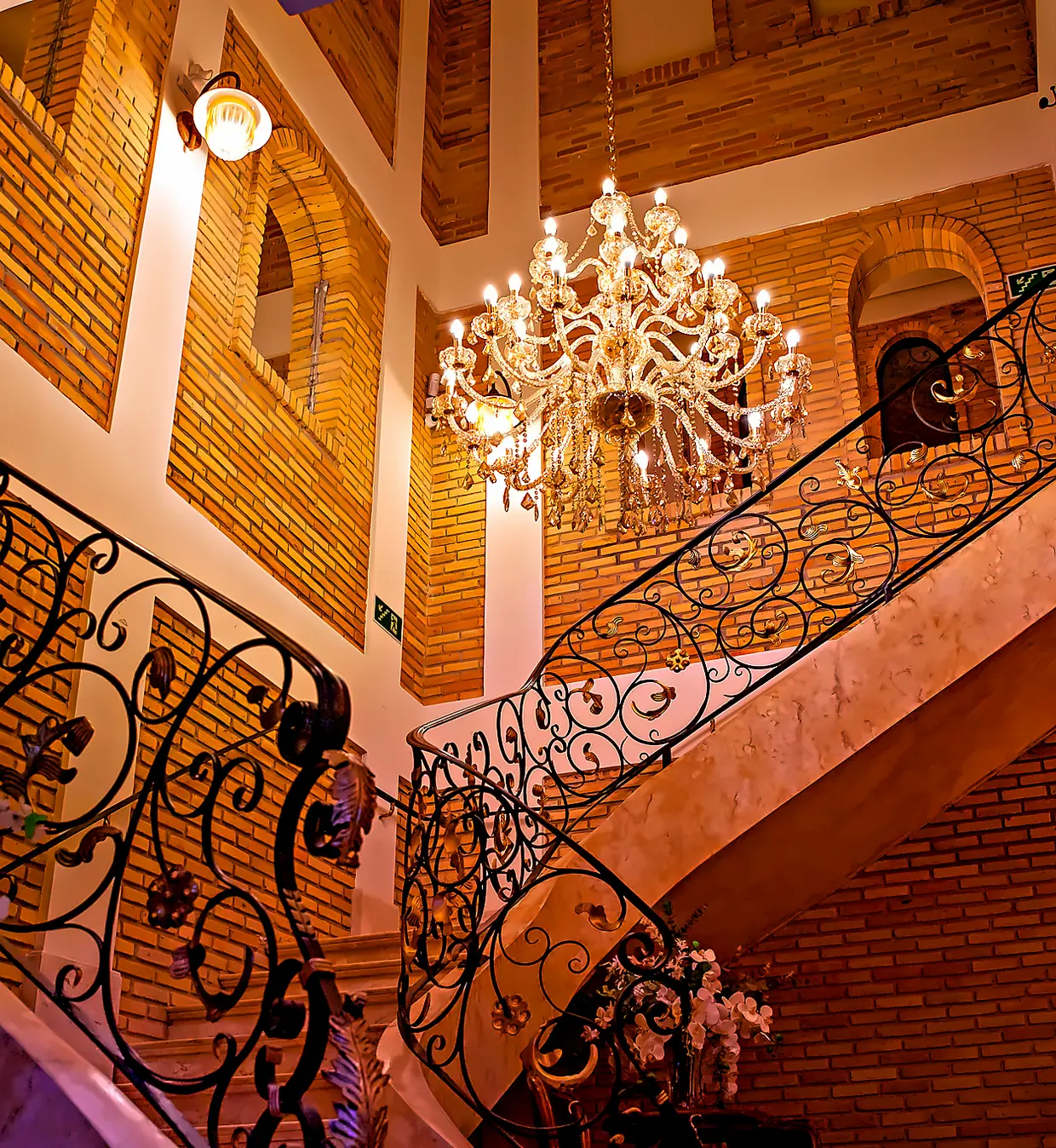 Escadaria curva de mármore sob o lustre de cristal, no pé-direito duplo da casa